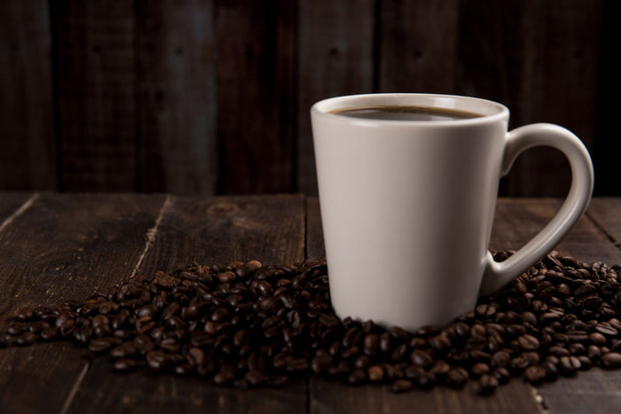 Tasse de café entourée de grains de café torréfiés sur une table en bois